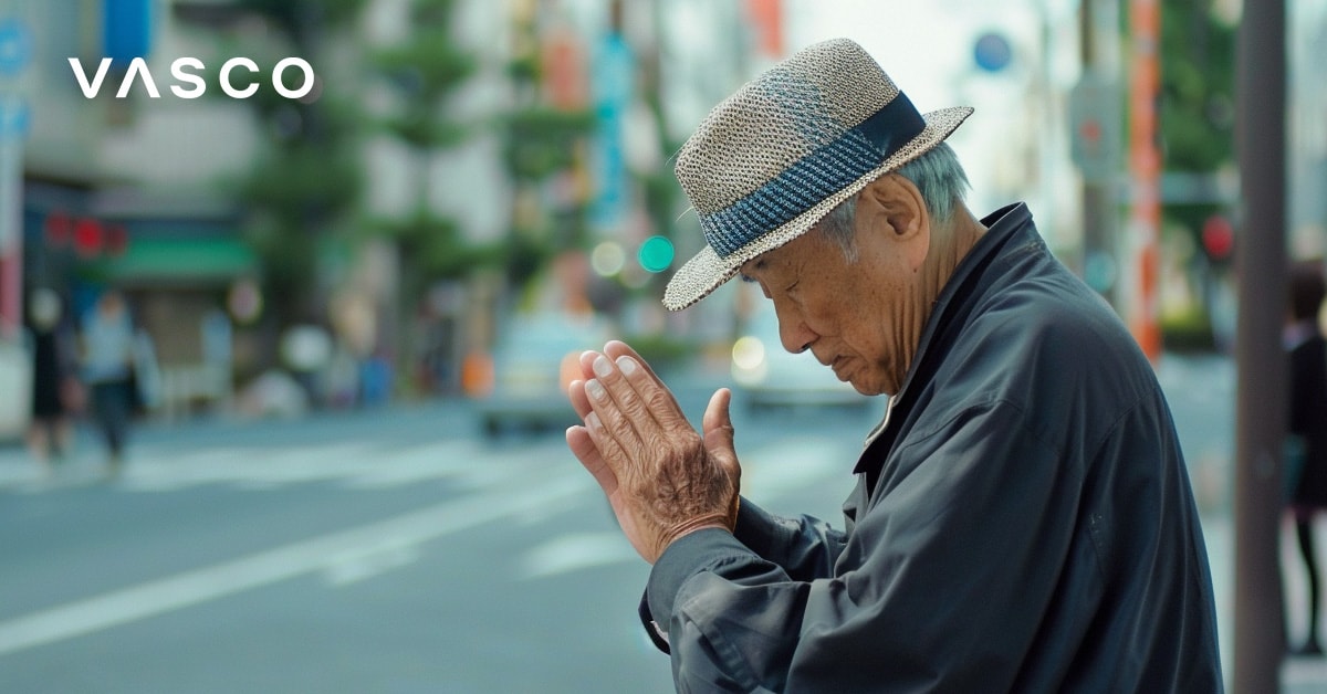 Egy idős férfi összekulcsolt kézzel meghajol, és a japán nyelvű köszöntést ábrázolja.