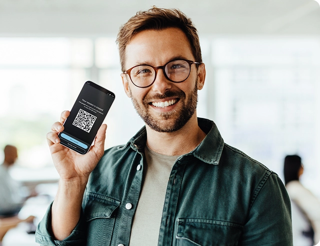Egy mosolygós férfi a kezében egy okostelefonnal, amelyen egy QR-kód látható a Vasco Audience csatlakozásához.