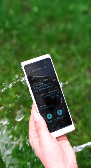 Közeli kép egy kézről, amint a Vasco Translator V4-et tartja, miközben víz fröccsen rá, kiemelve annak tartósságát.