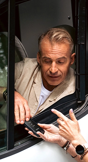 Egy férfi ül egy autóban, és a Vasco Q1 készülékhez beszél, amit valaki átnyújt neki.