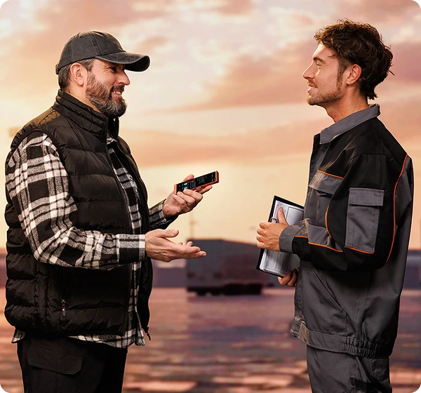 Két férfi beszélget egymással; a teherautó-sofőr egy Vasco Translator V4-et tart a kezében, a szemben álló személy, aki raktári munkásnak tűnik, dokumentumokat tart. A Vasco Translator segítségével kommunikálnak.