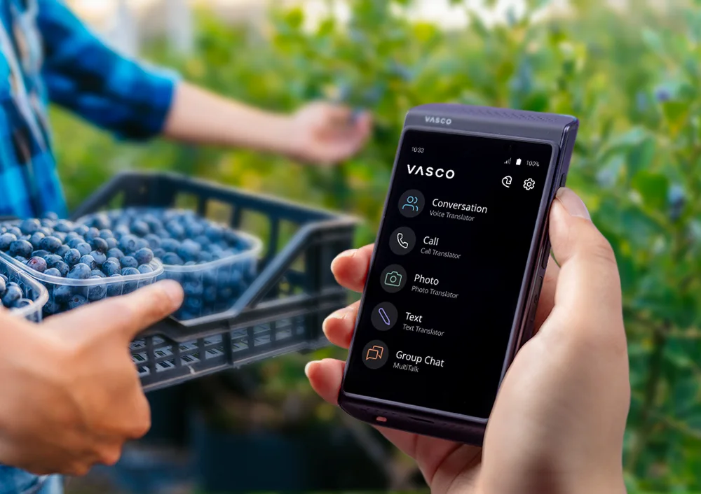Előtérben a Vasco Translator Q1, háttérben áfonyabokrokkal és egy leszedett áfonyával teli ládát tartó személlyel.