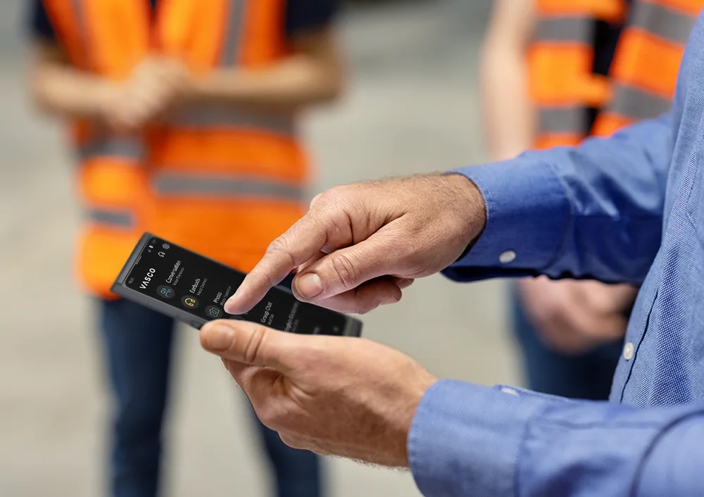 Egy Vasco V4-est tartó személy, a háttérben munkaruhás emberek láthatók.