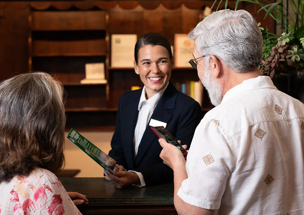 Egy mosolygó recepciós a Vasco Translator V4-es verziójával készült fordítást hallgatja, amelyet egy feléje irányított férfi tart a kezében.