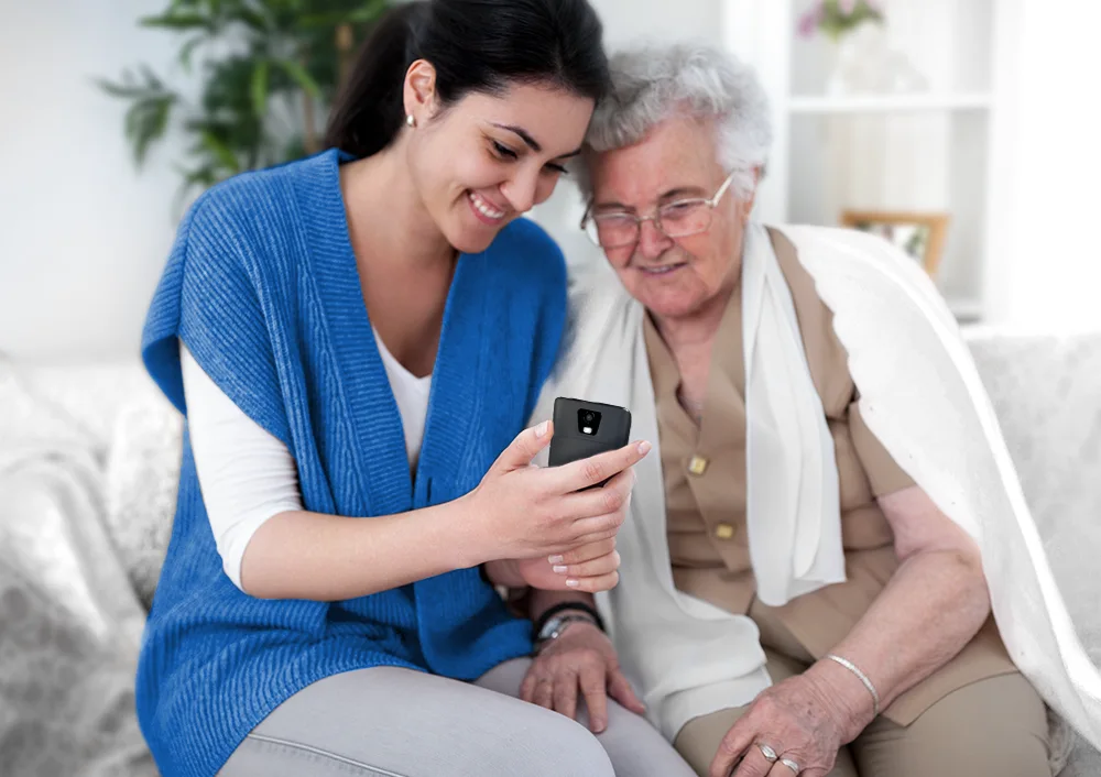 Egy nő egy Vasco Translator Q1-et mutat egy idős nőnek, demonstrálva annak használatát idősek segítésére.