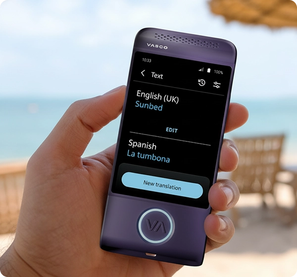 Közelkép egy kézről, amely egy lila színű Vasco elektronikus fordítógépet tart. A képernyőn egy szövegfordítás látható angol (brit) nyelvről spanyolra, amelyben a „Sunbed” szó fordítása „La tumbona”. A háttérben egy ragyogó, napsütötte tengerparti táj látható, ahol a tenger, az aranyszínű homok, több napozóágy és egy szalmából készült napernyő lágy fókuszú képe tárul elénk. 
