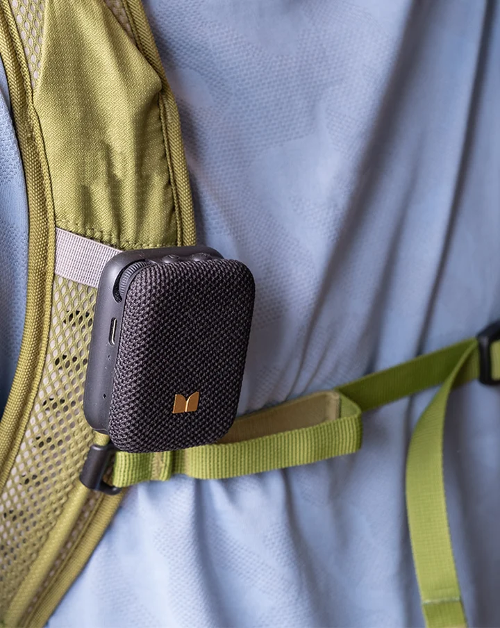 Fekete mini Bluetooth-hangszóró, amely egy hátizsák olajzöld pántjára van rögzítve
