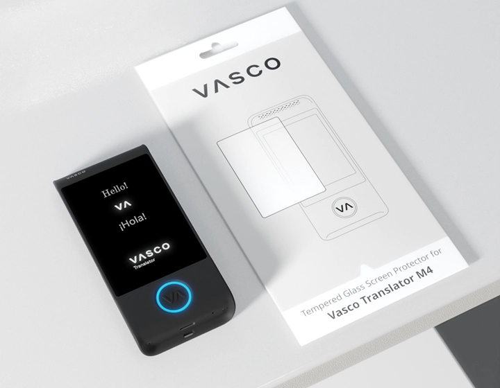 Vasco Translator M4, a Vasco logós gombján világító kék LED-del, egy asztalon a Vasco Translator M4 hordozható fordítógép képernyővédő fóliájának csomagolása mellett.