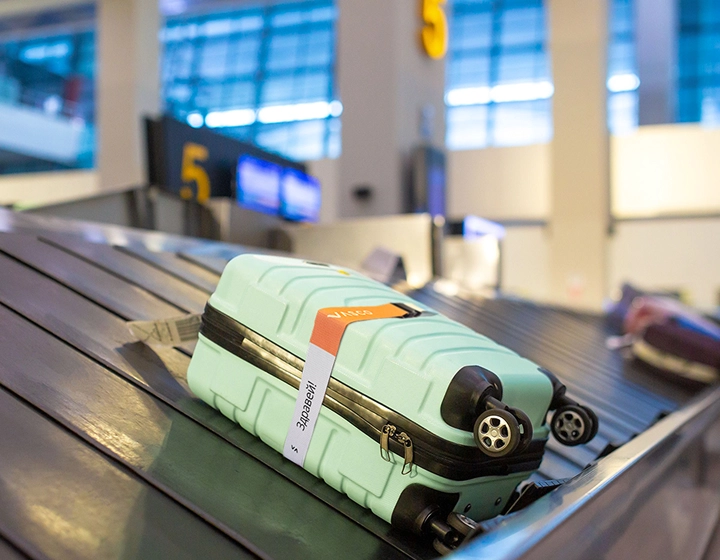 Green suitcase with a rainbow Vasco security strap lying on an airport baggage carousel. The colorful strap makes the suitcase easy to recognize.